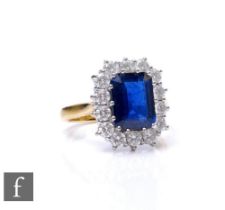 An 18ct hallmarked sapphire and diamond cluster ring, emerald cut sapphire, weight 3.36ct, within