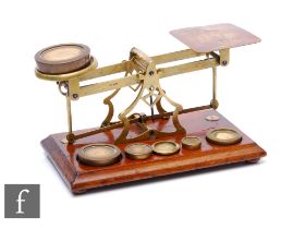 A set of Edwardian brass postal scales with associated weights, on mahogany plinth base, width 28cm.