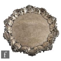 A hallmarked silver circular salver with engraved decoration within raised scroll decorated