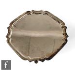 A hallmarked silver canted square salver with stepped borders and raised on four scroll feet, weight