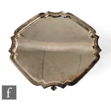 A hallmarked silver canted square salver with stepped borders and raised on four scroll feet, weight