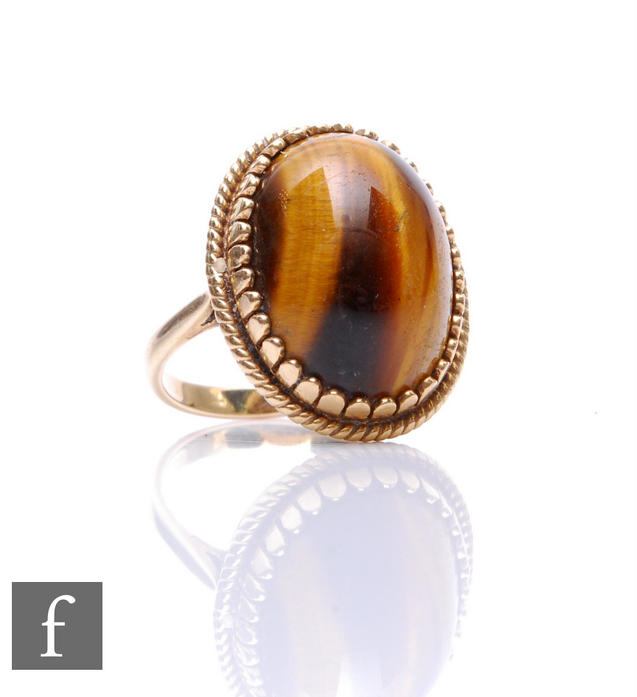 An 9ct hallmarked single stone oval tigers eye ring, cabochon cut stone within rope twist border,