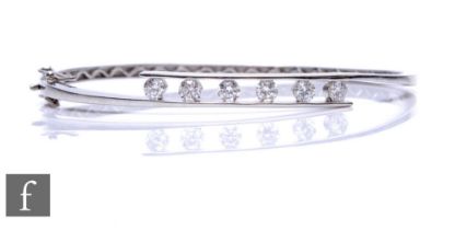 An 18ct hallmarked white gold hinged bangle, part channel set with six brilliant cut diamonds, total