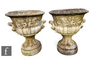 A large pair of reconstituted stone garden urns, each of pedestal form relief cast with putti,