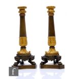 A pair of 19th Century French Empire bronze and gilt metal candlesticks, part reeded and leaf scroll
