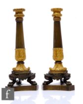 A pair of 19th Century French Empire bronze and gilt metal candlesticks, part reeded and leaf scroll