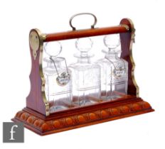 An Edwardian carved oak three bottle tantalus each with square cut glass decanters and two labels '