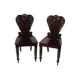 A pair of William IV Irish mahogany Hall Chairs, with carved shield backs over solid seats on