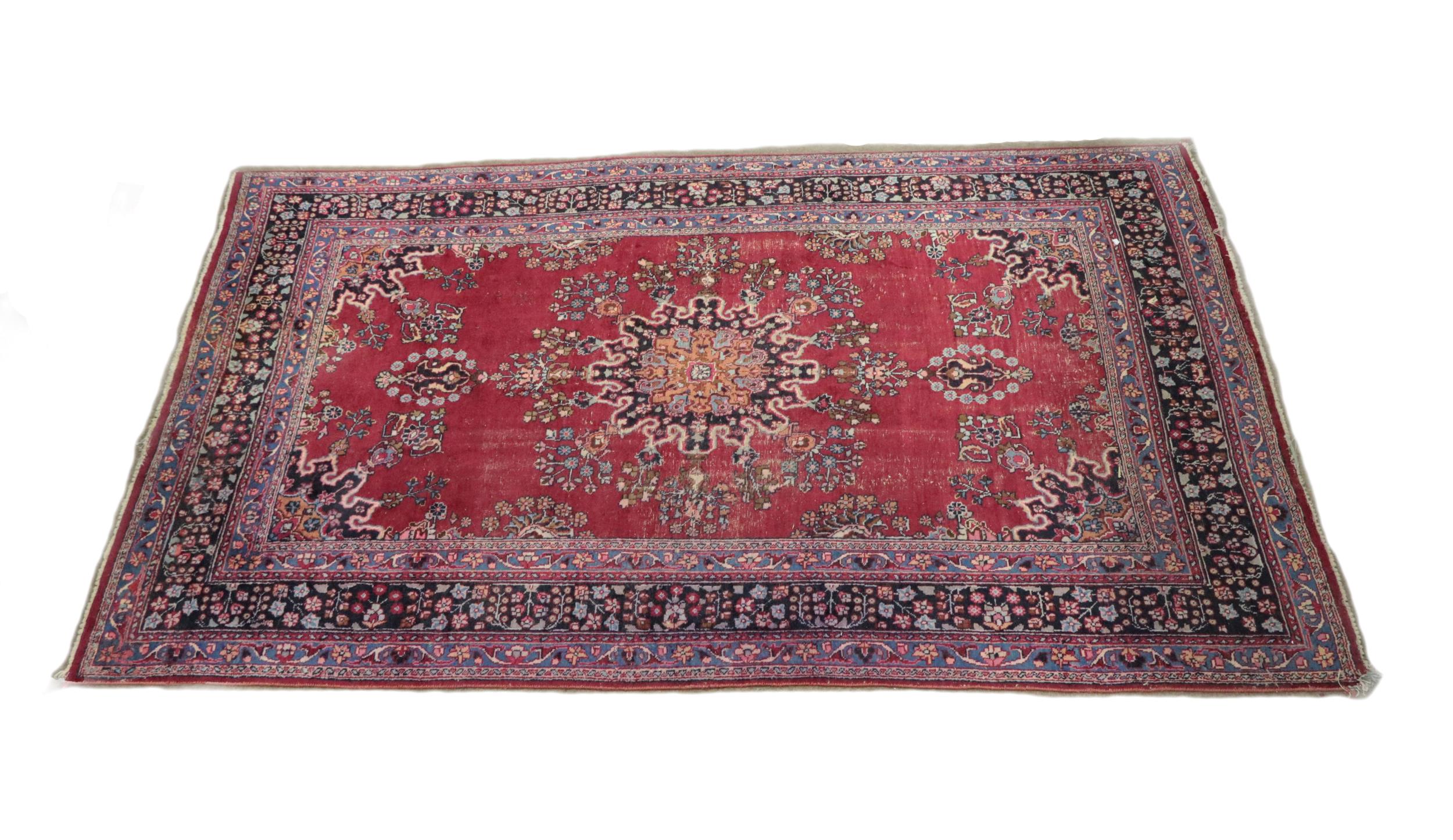 A large semi-antique Middle Eastern design burgundy ground woolen Carpet, the centre section with