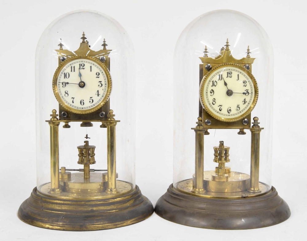 Two similar brass torsion timepieces with disc pendulums, under glass domes and upon circular