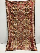 An antique Anatolian Kilim carpet woven eight octagonal medallions on a brick red ground, 266cm x