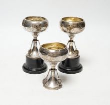 A set of three small George V silver tennis related trophy cups, with racket supports and engraved