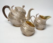 A 20th century Indian three piece embossed white metal tea set, with boteh and cobra decoration,