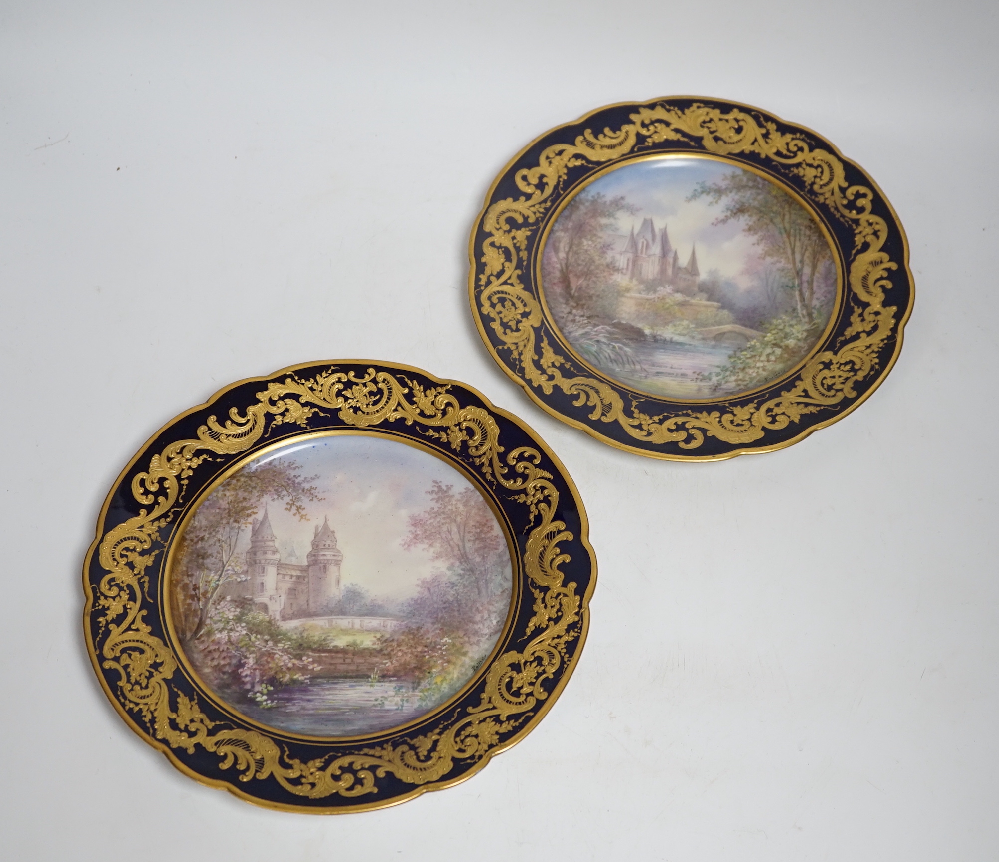 A pair of Sevres style blue cabinet plates, each decorated with a chateau, 24.5cm diameter
