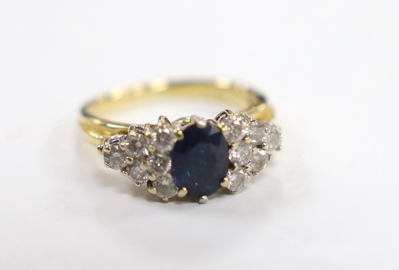 A modern 18ct gold and single stone oval cut sapphire set dress ring, with twelve stone diamond