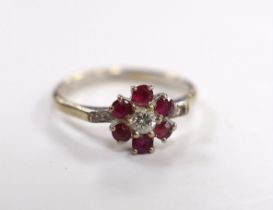 An 18ct white metal, ruby and diamond cluster set flower head ring, with diamond chip set shoulders,
