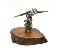 A vintage chrome plated car mascot of a winged female riding a wheel, mounted on a tree trunk
