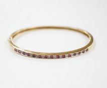 A yellow metal, ruby and diamond chip channel set hinged bangle, interior diameter 57mm, gross