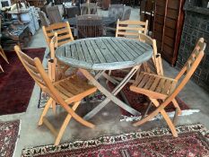 A circular weathered teak garden table, diameter 111cm, height 73cm with four folding hardwood