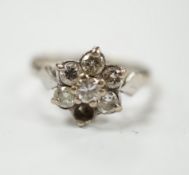 An 18ct white metal and seven stone diamond cluster set flower head ring (one stone missing), size