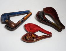 Three cased pipes, one with carved amber novelty bowl, the other two with amber pipe ends, metal