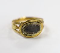 An early 19th century two colour yellow metal mourning ring, with glazed panel and pierced foliate