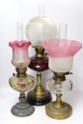 Three oil lamps with glass reservoirs and shades, one with Art Nouveau style base, 62cm high