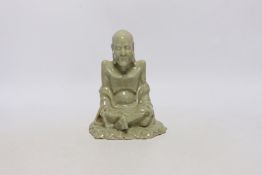 A Chinese celadon glazed figure of Laozi, 18th / 19th century, cross-legged and seated on leaves,