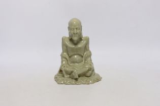 A Chinese celadon glazed figure of Laozi, 18th / 19th century, cross-legged and seated on leaves,