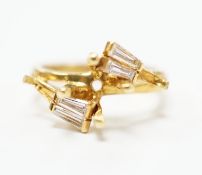 A modern 18ct gold and four stone trapeze cut diamond set crossover ring, size J, (central stone