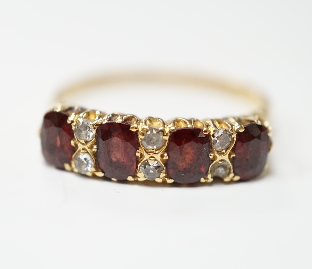 An Edwardian 18ct gold and four stone garnet set half hoop ring, with diamond chip spacers, size