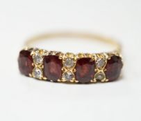 An Edwardian 18ct gold and four stone garnet set half hoop ring, with diamond chip spacers, size