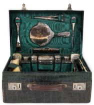 A George V green crocodile toilet case, fitted with fifteen silver mounted toilet jars and