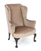 A George II style mahogany wing armchair, upholstered in beige dralon, on acanthus kneed cabriole