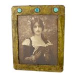An Arts & Crafts brass picture frame, of rounded rectangular form, the top inset with three
