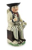 A Staffordshire pearlware sailor Toby jug, c.1800-10, seated on a sea-chest, holding a cup in his