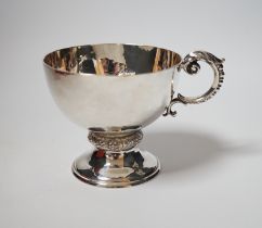 A George V planished silver pedestal single handled cup, Goldsmiths & Silversmiths Co Ltd, London,