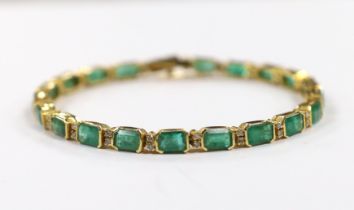 A modern 18k yellow metal and twenty stone emerald set line bracelet, with diamond chip spacers,