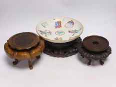 A Chinese famille rose dish and three carved hardwood stands, largest 23cm in diameter
