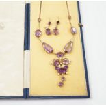 An early 20th century yellow metal, amethyst and enamel set suite of jewellery, comprising a drop