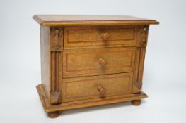A miniature oak chest of drawers and contents (miniature bisque headed dolls and linen) height 22cm