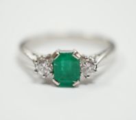A modern 18ct white metal, single stone emerald and two stone diamond set ring, size N, gross weight