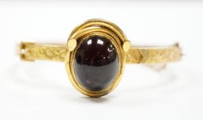A late Victorian 9ct gold and single stone cabochon red paste set hinged bangle, gross weight 14.5