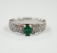 A modern 18ct white gold and single stone oval cut emerald set ring, with pave set diamond