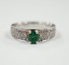 A modern 18ct white gold and single stone oval cut emerald set ring, with pave set diamond