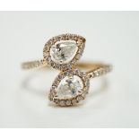 A modern 18k and two stone pear cut diamond set cross-over ring, with diamond chip border and