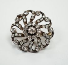 A Victorian yellow metal and diamond cluster set whorl shaped brooch, scrolling border and