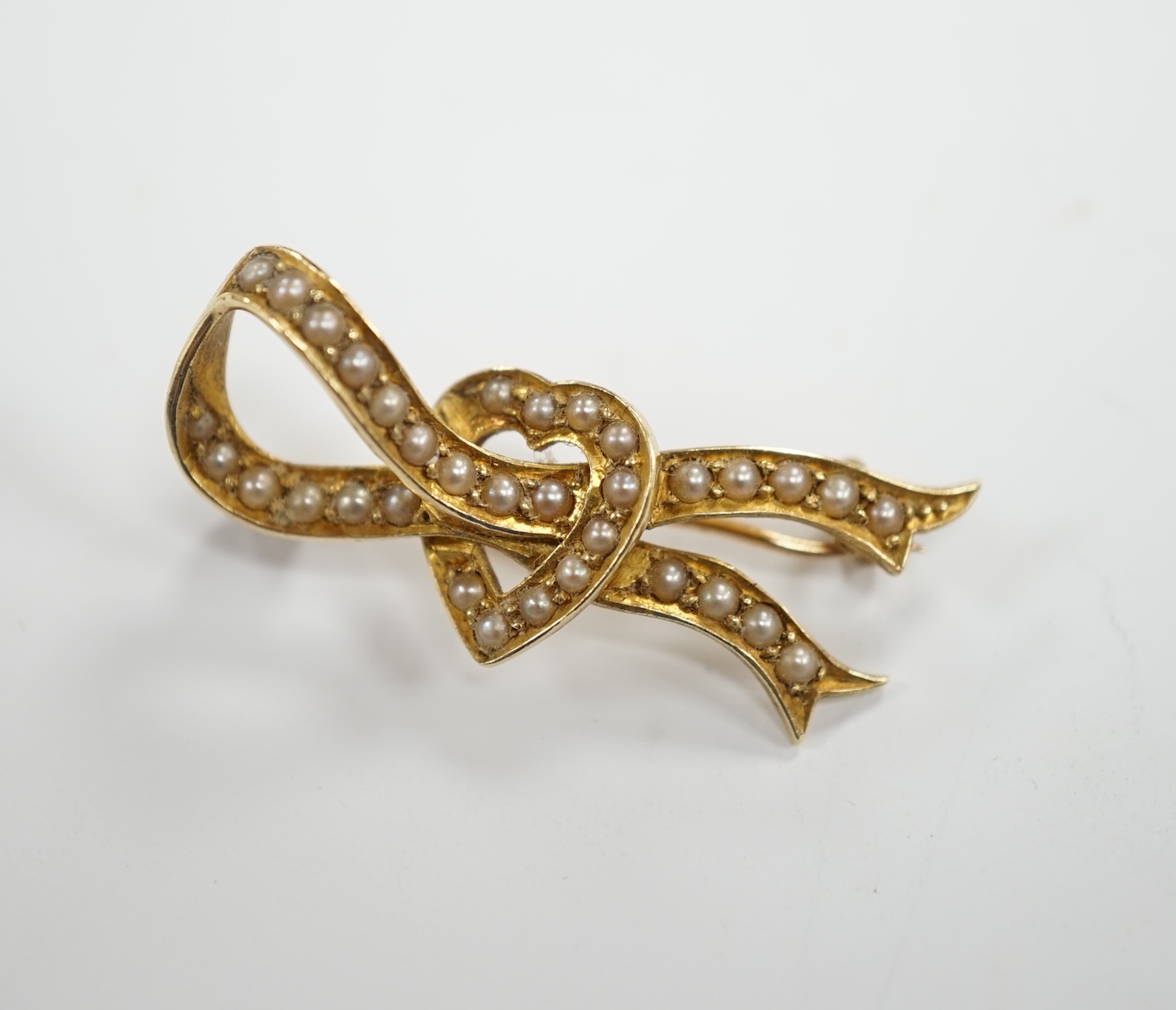 An Edwardian yellow metal and seed pearl cluster set ribbon and heart brooch, 34mm, gross weight 4.3