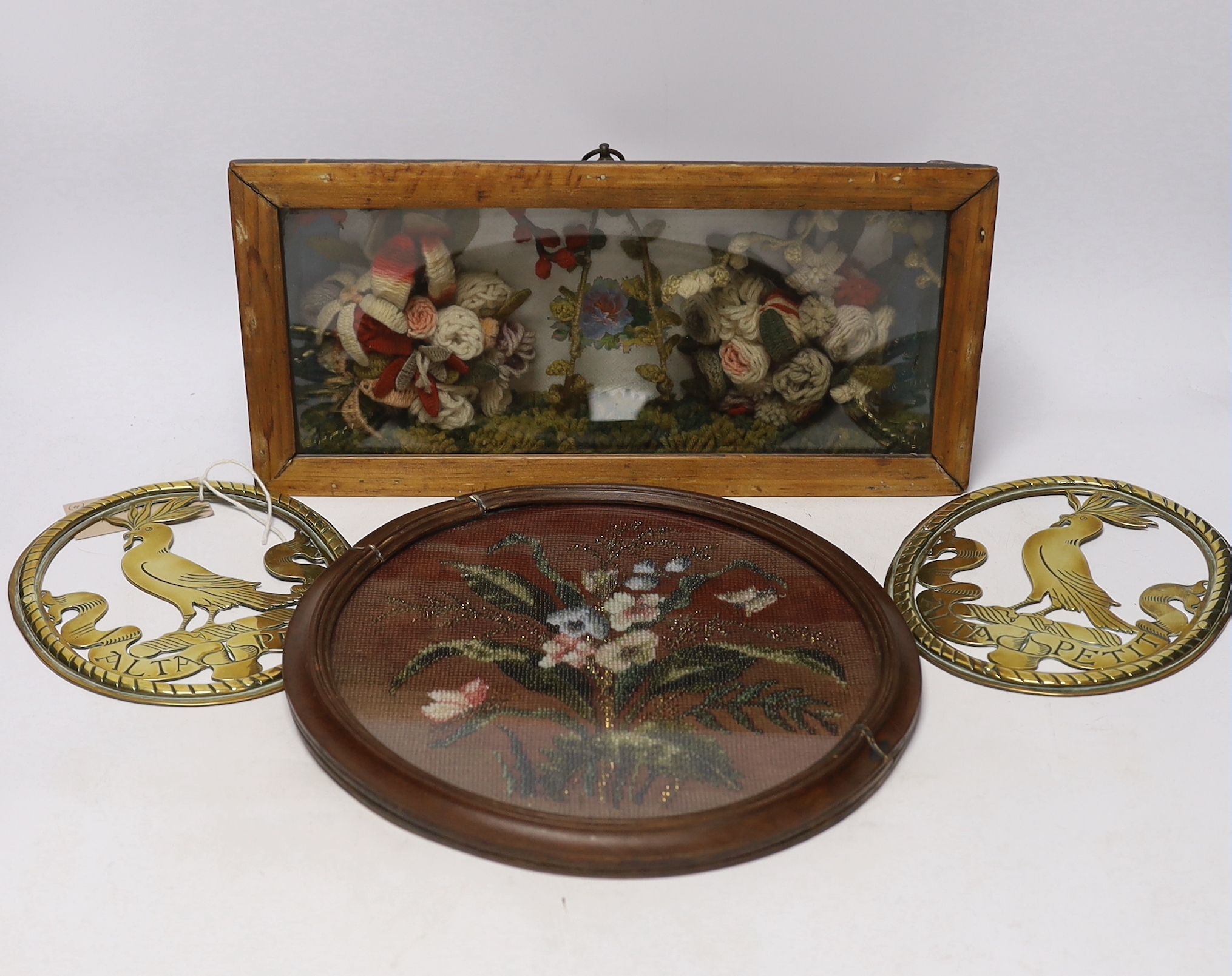 A pair of oval brass crests, a circular framed Berlin beadwork panel and a framed floral wool work