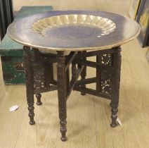 A Persian brass engraved tray top table on folding carved wood base, 59cm in diameter